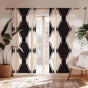 May include: Cream-colored curtains with a bold black geometric pattern hang in front of a window. The pattern consists of repeating arrow-like shapes. The curtains are hung on a wooden rod. A large potted plant and a hanging plant are visible.