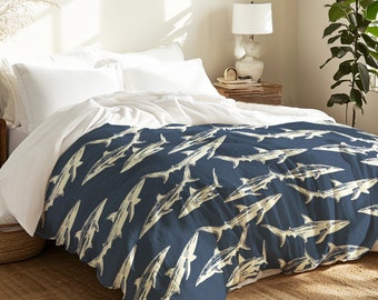 May include: A blue and white duvet cover with a repeating pattern of sharks. The duvet cover is on a bed with white pillows and a white blanket.