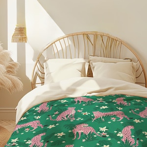 Könnte beinhalten: Ein grüner und rosafarbener Leoparden-Druck-Bettbezug mit einem weißen Bettüberwurf und zwei weißen Kissen auf einem Bett mit einem geflochtenen Korb-Kopfteil.