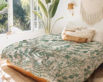 May include: A bed with a white and green floral duvet cover featuring a fern pattern. The bed is made with white pillows and a brown throw pillow. A large green plant is in the background.