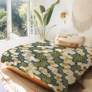 Pode incluir: Uma capa de edredom azul-esverdeado e dourado com um padrão repetitivo de flores brancas estilizadas. A capa de edredom está em uma cama com almofadas brancas e marrons.