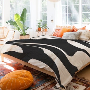 May include: A white and black patterned duvet cover with a modern abstract design. The duvet cover is on a bed with a wooden frame and is styled with throw pillows.