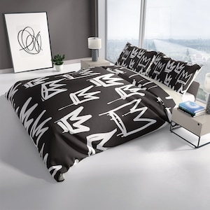May include: Black and white duvet cover with a repeating pattern of crown shapes. The duvet cover is on a bed with two white pillowcases with a crown pattern.