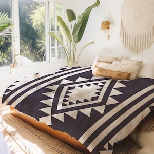 May include: A black and white geometric patterned duvet cover with a large diamond shape in the centre. The duvet cover is on a bed with a wooden frame and a tan rug.
