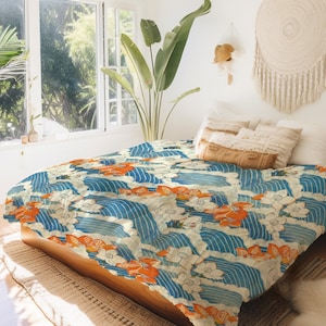 以下が含まれることがあります： 青と白の布団カバーで、花柄と波のデザインが施されています。布団カバーは、白い枕と茶色の枕のあるベッドの上に置かれています。