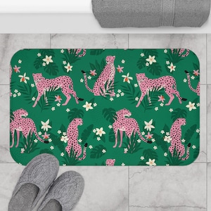 Op de afbeelding: Een groene badmat met een roze luipaardprint. De luipaardprint wordt herhaald over de hele mat en heeft roze luipaard-silhouetten op een groene achtergrond met witte bloemen.
