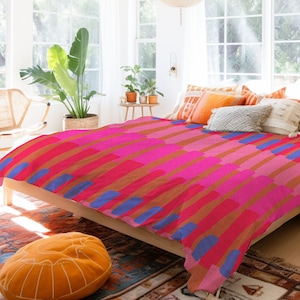 Puede incluir: Una funda nórdica con estampado geométrico rosa, rojo y azul sobre una cama con estructura de madera. La funda nórdica tiene un diseño moderno y abstracto.