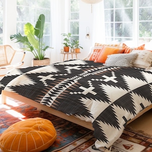 Puede incluir: Una cama con una funda nórdica con estampado geométrico en blanco y negro. La funda nórdica tiene un color de acento marrón. La cama está decorada con almohadas en tonos naranja y crema.