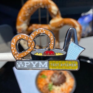 Puede incluir: Un pin de plata con un pretzel, un tazón de comida y el texto "P.Y.M. Test Kitchen".