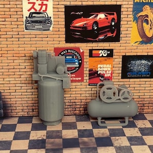 May include: Two gray air compressors, one with a large tank and the other with a smaller tank and a belt drive. The compressors are on a black and white checkered floor.