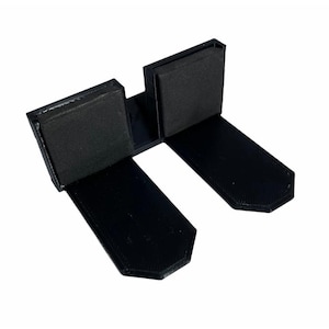 May include: A black U-shaped bracket featuring two parallel flat extensions and two vertical upright panels. Each vertical panel is lined with a rectangular black foam pad on the inner surface. The object is constructed from a solid black material.
