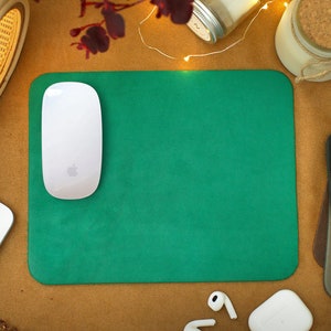 Peut inclure: Un tapis de souris vert avec une souris sans fil blanche sur le dessus. Le tapis de souris est sur une surface brune avec une lampe blanche, un bocal en verre et une bougie en arri&egrave;re-plan.