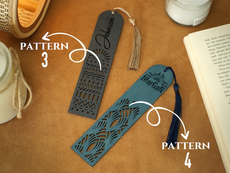 May include: Two wooden bookmarks with different patterns and tassels. The bookmark on the left has a black background with a geometric pattern and the text "Johnson" on it. The bookmark on the right has a blue background with a floral pattern and the text "Morgan" on it.
