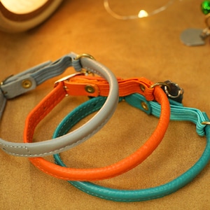 May include: Three leather pet collars in grey, orange and teal. The collars are stitched and have metal hardware.