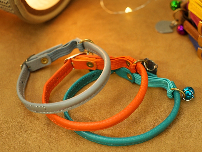 May include: Three leather pet collars in grey, orange and teal. The collars are stitched and have metal hardware.