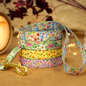 May include: A colorful dog leash with a floral pattern. The leash is made of multiple layers of fabric, each with a different floral design. The leash has a gold metal clip.