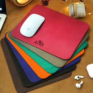 Peut inclure: Une pile de huit tapis de souris en cuir personnalis&eacute;s dans diff&eacute;rentes couleurs, dont le marron, le bleu marine, l'orange, le vert, le gris et le rouge. Le tapis de souris du dessus porte les initiales "ANB" en relief blanc.