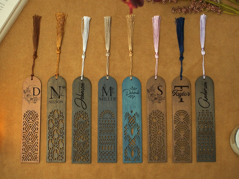 May include: Eight wooden bookmarks with laser-cut designs and personalized names. The bookmarks have tassels in various colors, including gold, white, pink, and blue.