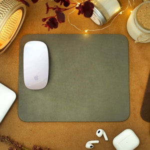 Peut inclure: Un tapis de souris gris avec une souris sans fil blanche sur le dessus. Le tapis de souris est sur une surface brune avec une lampe en bambou, un bocal en verre avec un couvercle en li&egrave;ge et une pile de coussinets en cuir color&eacute;s.