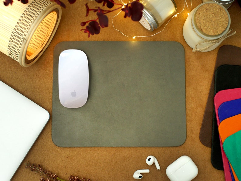 Peut inclure: Un tapis de souris gris avec une souris sans fil blanche sur le dessus. Le tapis de souris est sur une surface brune avec une lampe en bambou, un bocal en verre avec un couvercle en li&egrave;ge et une pile de coussinets en cuir color&eacute;s.