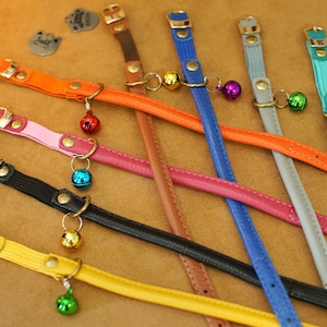 May include: Assortment of colourful leather cat collars with small bells attached. The collars are in various colours, including orange, pink, black, yellow, brown, blue, and grey.