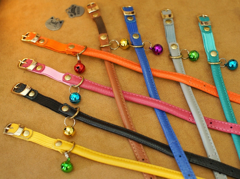 May include: Assortment of colourful leather cat collars with small bells attached. The collars are in various colours, including orange, pink, black, yellow, brown, blue, and grey.