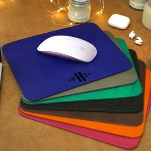 Peut inclure: Une pile de tapis de souris en cuir de diff&eacute;rentes couleurs avec une souris sans fil blanche sur le dessus du tapis de souris bleu. Le tapis de souris du dessus porte les initiales "D.H.S." en lettres noires.