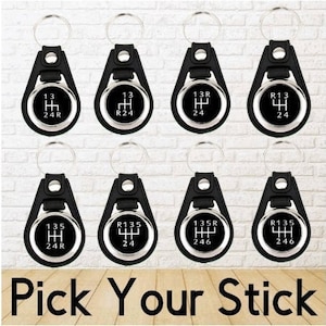 May include: Eight black leather keychains with silver metal rings and circular inserts featuring different gear shift patterns. The inserts show the gear shift patterns for 13, 13R, 135, and 135R gearboxes. The text "Pick Your Stick" is displayed below the keychains.