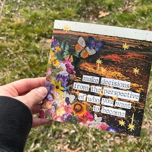 May include: A colorful card with a floral and butterfly design, featuring the text "make decisions from the perspective of who you want to become." The card has a mix of vibrant colors and a nature-inspired theme.