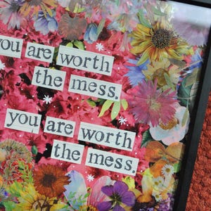 May include: A framed floral collage with a black border. The artwork features a vibrant mix of colorful flowers and the text "you are worth the mess." The background is a blend of pink and red hues.