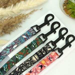 May include: Four colourful dog leads with black metal clips. The leads feature different patterns, including a floral design, a celestial pattern, and a geometric pattern.