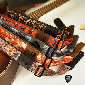 May include: Five colorful guitar straps with different patterns and designs. The straps are made of fabric and have leather accents. The straps are all personalized with names, including "Lucas", "Oliver", and "Mia".