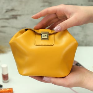 Könnte beinhalten: Eine kleine, senfgelbe Ledertasche mit einem goldenen Verschluss und den eingravierten Initialen "VN" auf der Vorderseite.