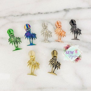 May include: Assortment of palm tree zipper pulls in various colors, including gold, silver, bronze, green, and iridescent. The zipper pulls are made of metal and feature a detailed palm tree design.