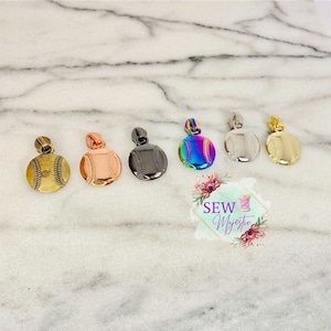 Puede incluir: Seis tiradores de cremallera de metal de diferentes colores con forma de pelota de béisbol. Los tiradores de cremallera están dispuestos en una fila de izquierda a derecha. Los colores son oro antiguo, oro rosa, negro, arcoíris, plata y oro.