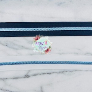 May include: Two zipper tapes, one black and one white, with a light blue zipper pull. The zipper tapes are on a marble background.