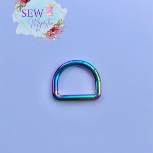Puede incluir: Un anillo en D de metal iridiscente arco&iacute;ris. El anillo es de tama&ntilde;o est&aacute;ndar para sujetar a bolsos, correas u otros accesorios.