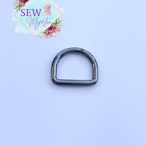 Puede incluir: Un anillo en D de metal negro, un accesorio com&uacute;n utilizado en proyectos de artesan&iacute;a y costura.