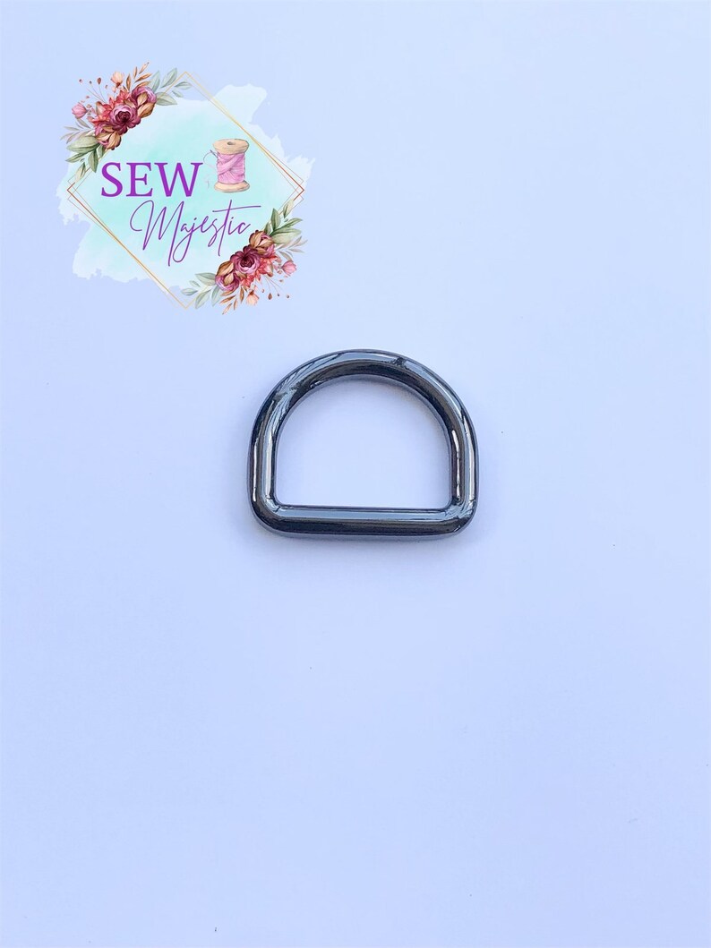 Puede incluir: Un anillo en D de metal negro, un accesorio com&uacute;n utilizado en proyectos de artesan&iacute;a y costura.