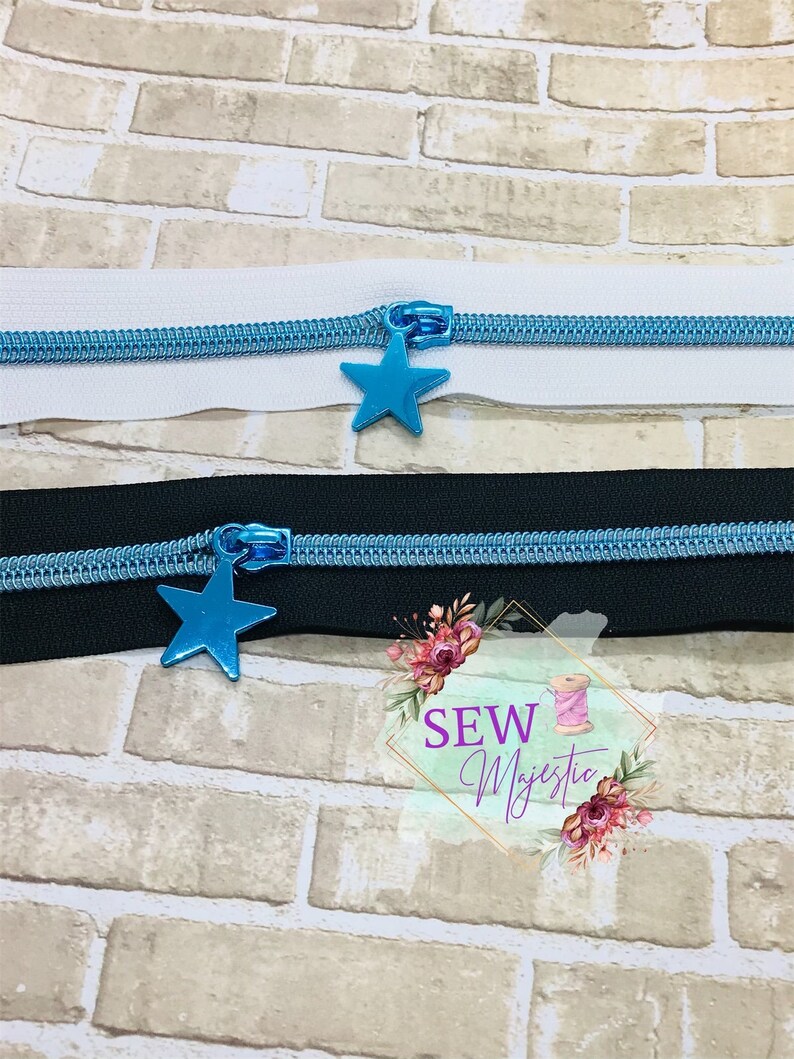 May include: Two zipper pulls with blue metal star charms. The zipper pulls are on white and black fabric.