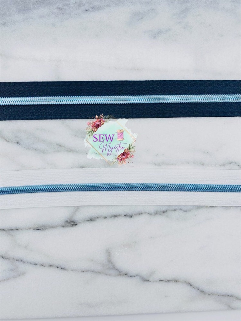 May include: Two zipper tapes, one black and one white, with a light blue zipper pull. The zipper tapes are on a marble background.