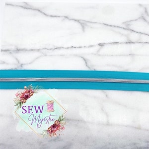 May include: A turquoise zipper with a silver slider on a white marble background. The text "SEW Majestic" is visible in the lower portion of the image.