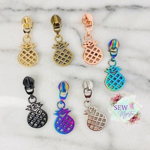 May include: Assortment of zipper pulls featuring a pineapple design. The pulls are available in gold, rose gold, silver, black, and rainbow.