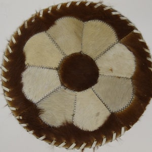 Może przedstawiać: Okrągły, brązowo-biały dywan skórzany z wzorem kwiatowym. Dywan wykonany jest z różnych kawałków skóry zszytych ze sobą.