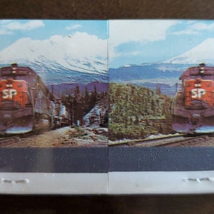 May include: A vintage postcard featuring a red and gray train engine with the letters "SP" on the side, traveling through a mountainous landscape with a snow-capped mountain in the background.