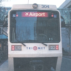 以下が含まれることがあります： 白とグレーのMAXレッドラインの電車で、前面に304の番号が書かれています。電車は駅に停車しており、正面ドアの上の標識には「空港」と表示されています。電車はTriMetシステムの一部です。