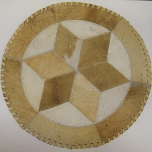 May include: A round, tan and white leather rug with a star-shaped design. The rug is stitched together with a tan thread.