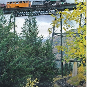 Peut inclure: Un train à vapeur d'époque traverse un pont en treillis dans un paysage montagneux. Le train est vert et noir avec une voiture de voyageurs jaune. Le texte "TRAIN RIDES" est sur une bannière dorée et rouge en haut de l'image. Le texte "GEORGETOWN LOOP HISTORIC MINING & RAILROAD PARK® 45 MILES WEST OF DENVER ON I-70" est en bas de l'image.