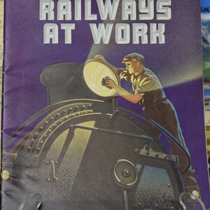 May include: A vintage book cover with a purple background and the text "RAILWAYS AT WORK" in white. The cover features a black and white illustration of a train engine with a worker cleaning the headlight.