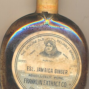 Può includere: Una bottiglia di vetro marrone scuro con un'etichetta che recita "The Genuine Old Reliable Brand. Ess. Jamaica Ginger Absolutely Pure. Franklin Extract Co. 130 Franklin St. N.Y."